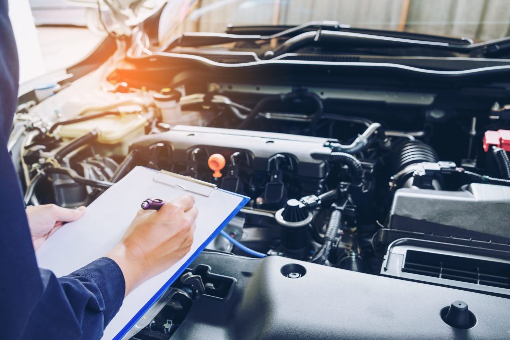 A mechanic holding a clipboard and pen while inspecting the engine of a car.